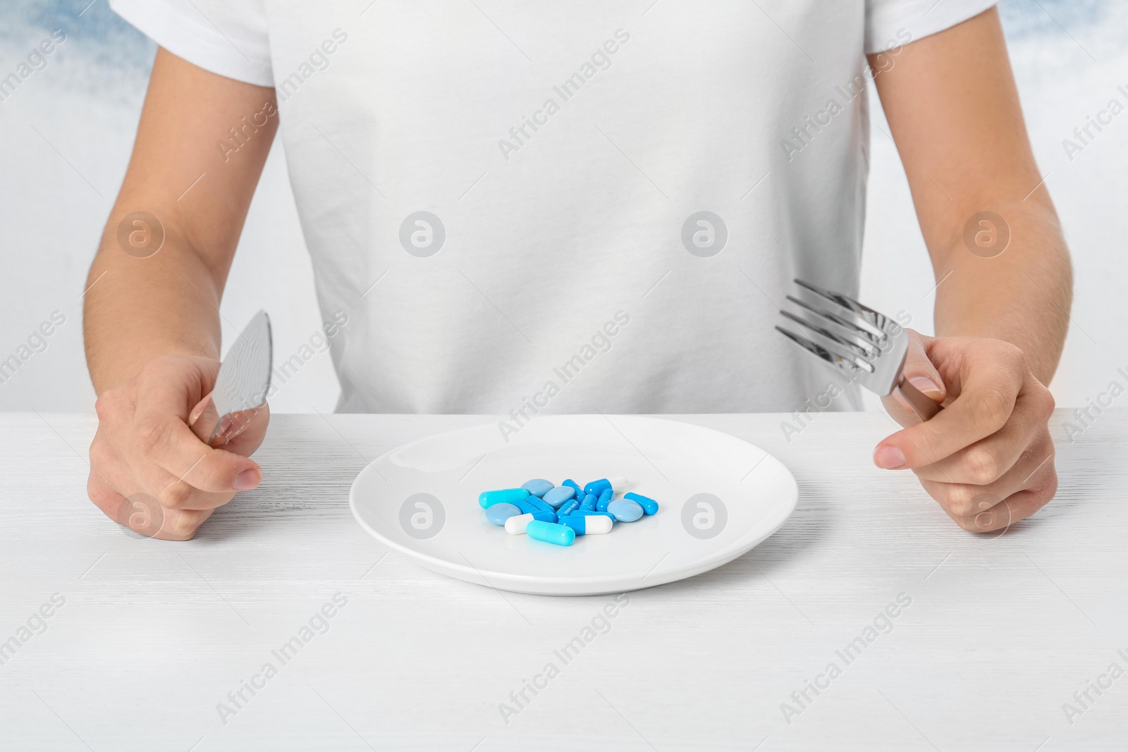 Photo of Woman sitting at table with cutlery and plate of weight loss pills, closeup