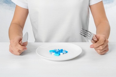 Woman sitting at table with cutlery and plate of weight loss pills, closeup