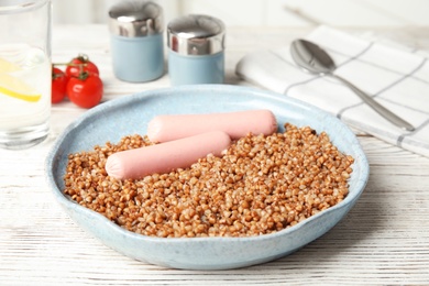 Photo of Delicious buckwheat porridge with sausages on white wooden table