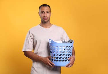 Young man with basket full of laundry on orange background