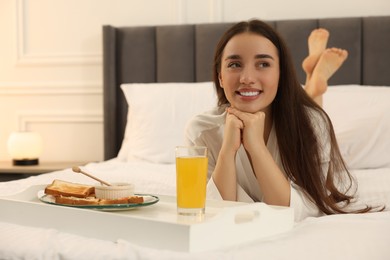 Photo of Happy young woman lying on bed near white tray at home