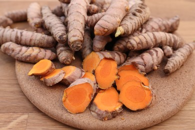 Photo of Board with fresh turmeric roots on wooden table, closeup