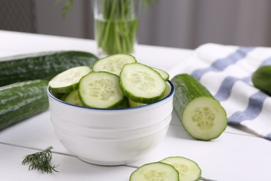 Cut cucumber in bowl, fresh vegetables and dill on white wooden table, closeup