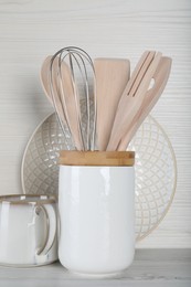 Photo of Holder with kitchen utensils, plate and mug on white wooden table