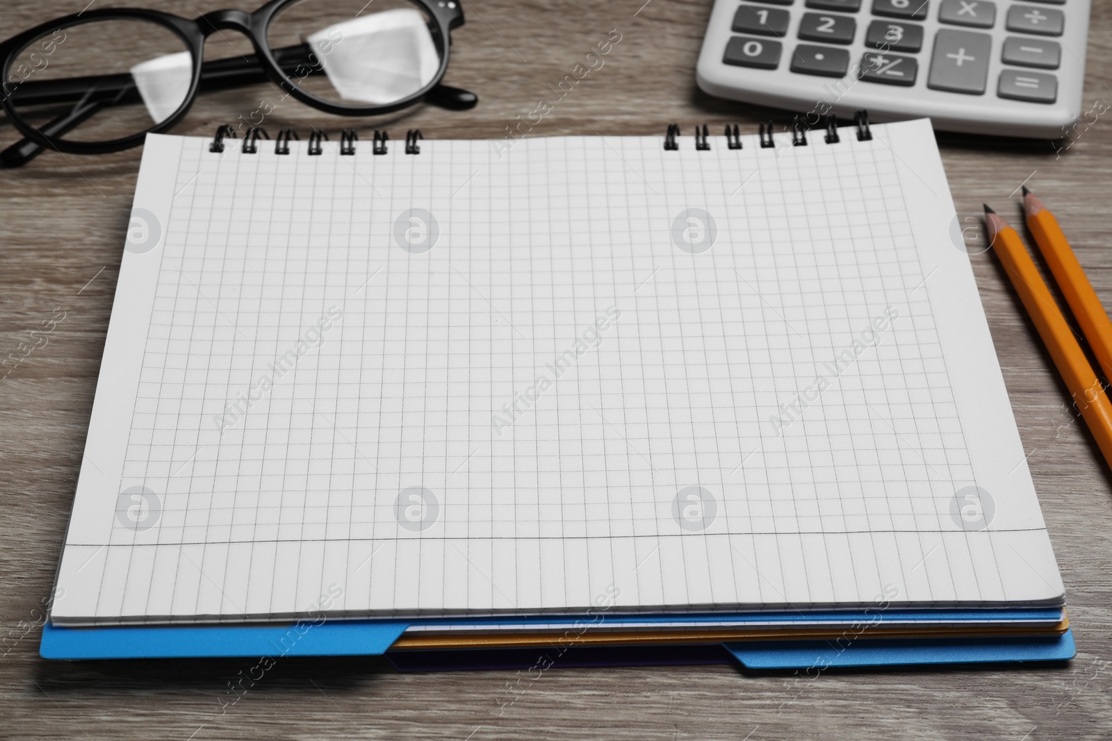 Photo of Empty notebook, calculator, glasses and pencils on wooden table, closeup