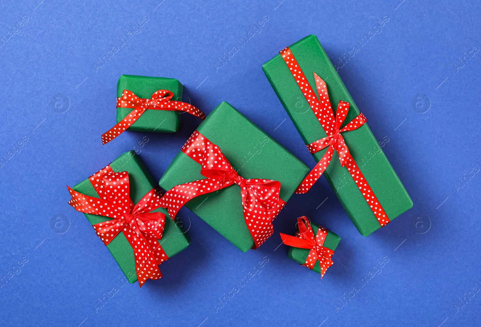 Photo of Christmas gift boxes with red bows on blue background, flat lay