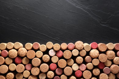 Many wine bottle corks on black table, flat lay. Space for text