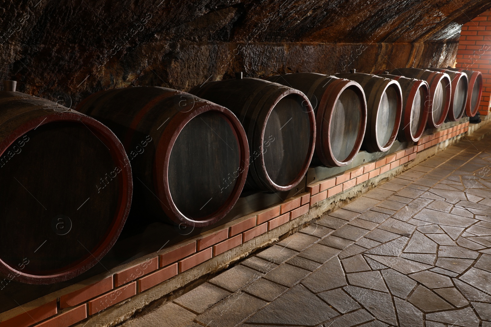 Photo of Many wooden barrels with alcohol drinks in cellar