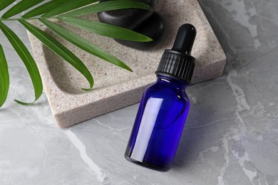 Photo of Bottle of face serum, soap dish, leaf and spa stones on grey marble table
