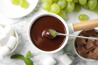 Photo of Dipping grape into fondue pot with dark chocolate on marble table, top view