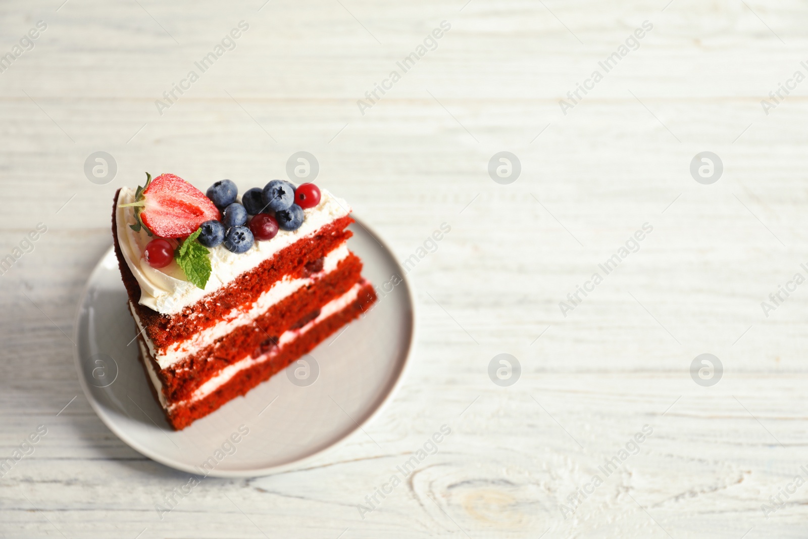 Photo of Plate with piece of delicious homemade red velvet cake and space for text on wooden table