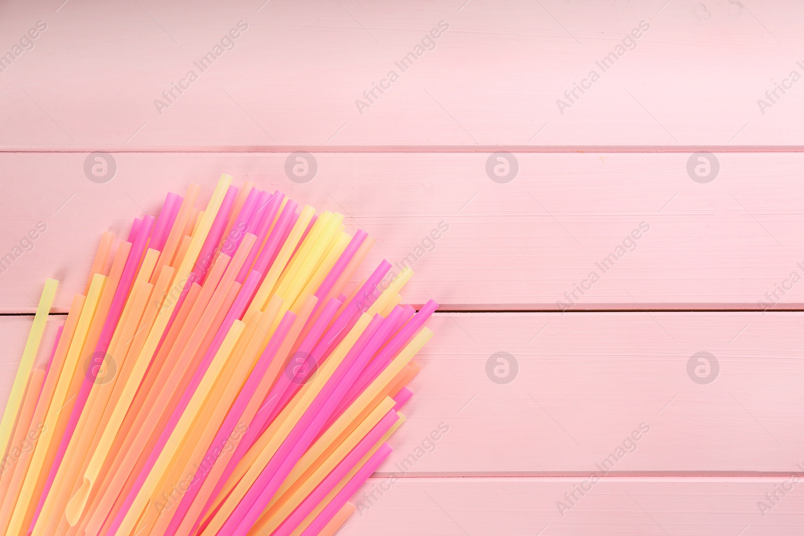 Photo of Colorful plastic drinking straws on pink wooden table, flat lay. Space for text