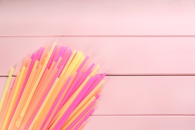 Photo of Colorful plastic drinking straws on pink wooden table, flat lay. Space for text