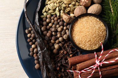 Plate with different aromatic spices and fir branches on light wooden table, top view