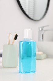 Bottle of mouthwash and toothbrushes on white table in bathroom