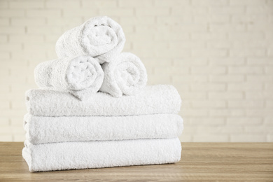 Clean bath towels on wooden table near white brick wall