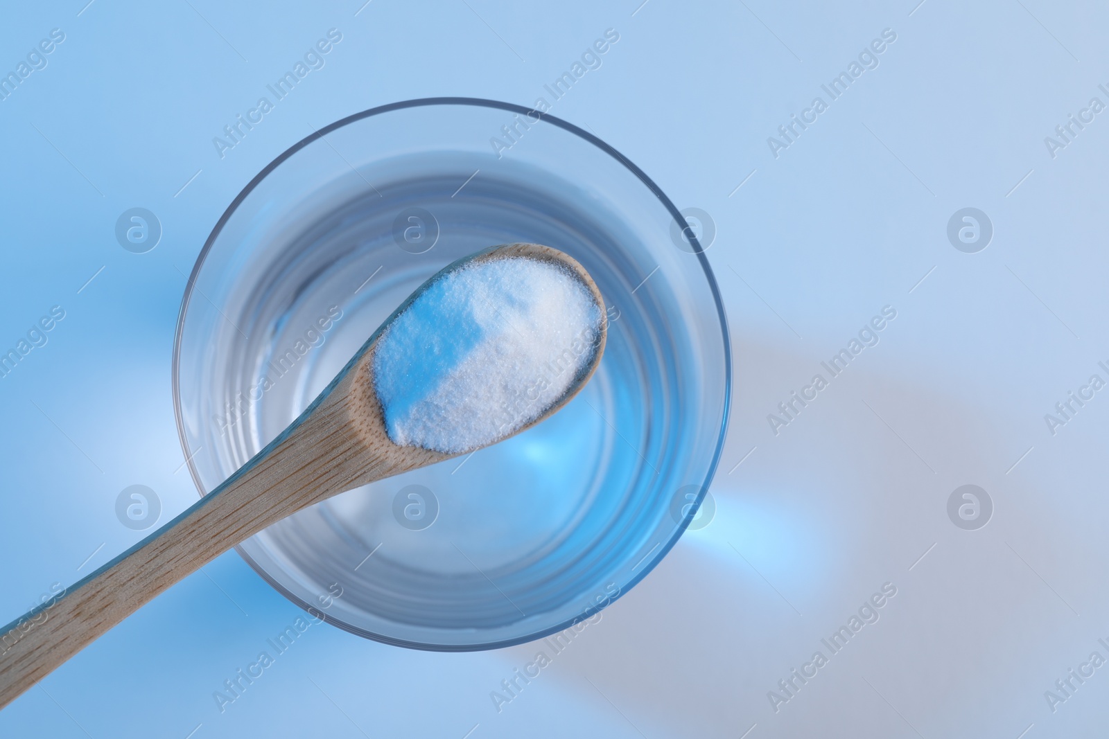 Photo of Spoon with baking soda over glass of water on light blue background, top view. Space for text