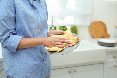 Woman wiping plate with towel in kitchen, closeup