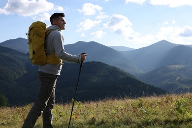 Tourist with backpack and trekking poles hiking through mountains, space for text