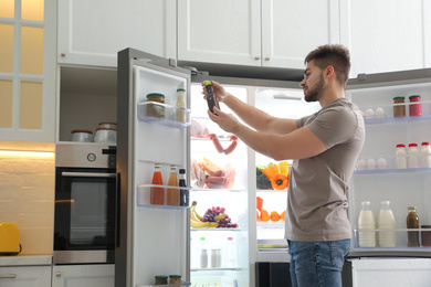 Photo of Young man with bottle of sauce near open refrigerator in kitchen