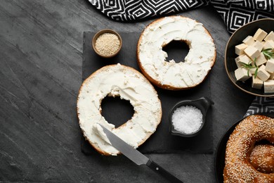 Photo of Delicious bagels with tofu cream cheese, sesame seeds and salt on black table, flat lay