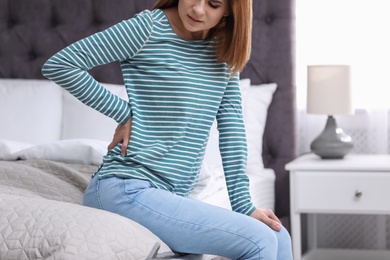 Photo of Young woman suffering from back pain at home, closeup