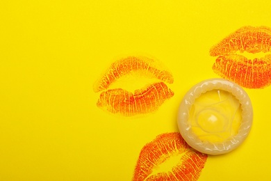 Condom with lipstick kiss marks and space for text on yellow background, top view. Safe sex