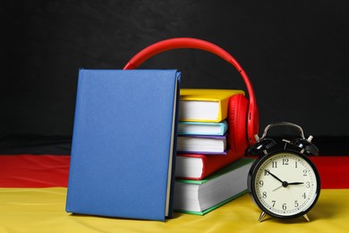 Photo of Learning foreign language. Different books, alarm clock and headphones on flag of Germany