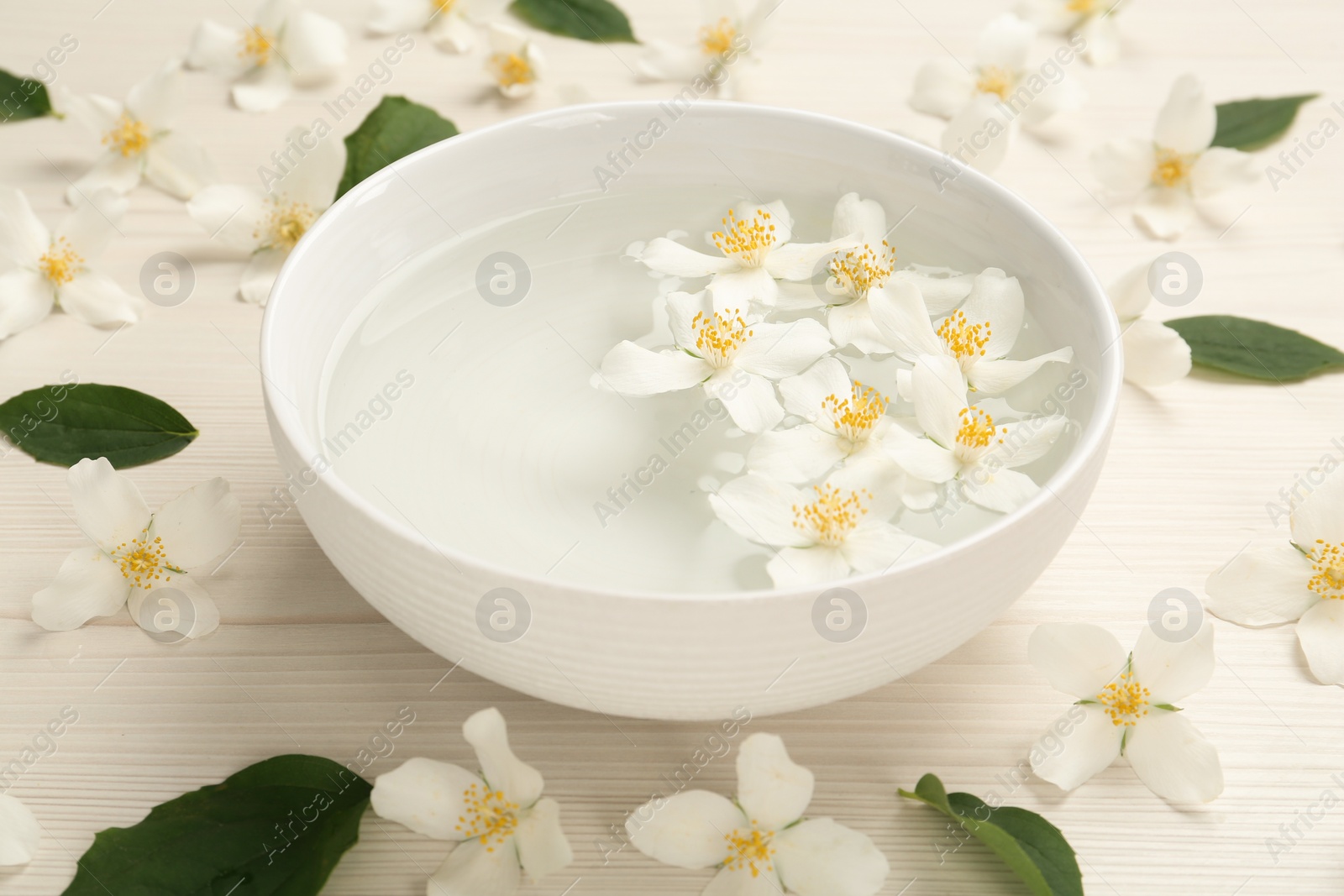 Photo of Bowl with water and beautiful jasmine flowers on white wooden table