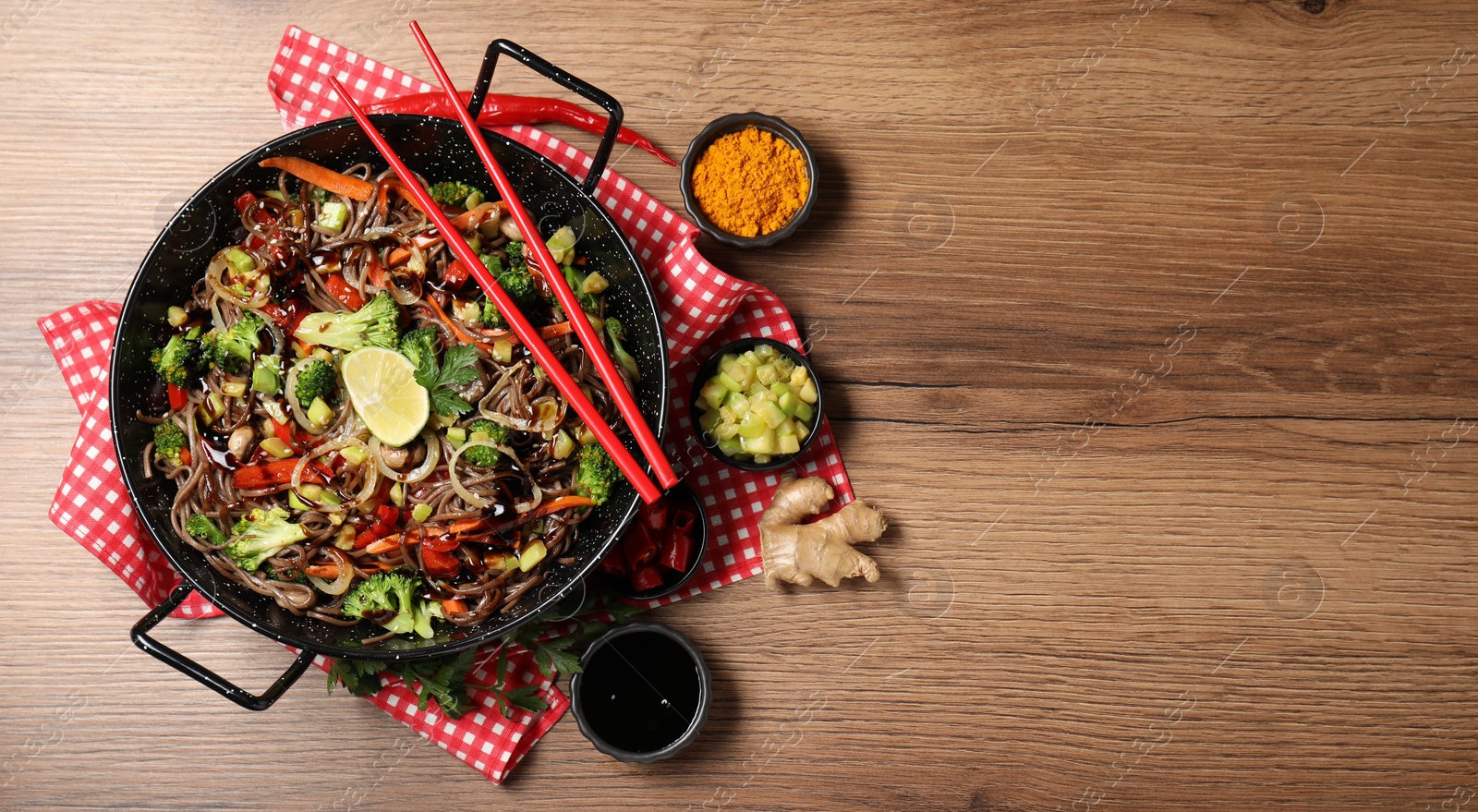 Photo of Stir-fry. Tasty noodles with meat in wok, chopsticks and ingredients on wooden table, flat lay. Space for text