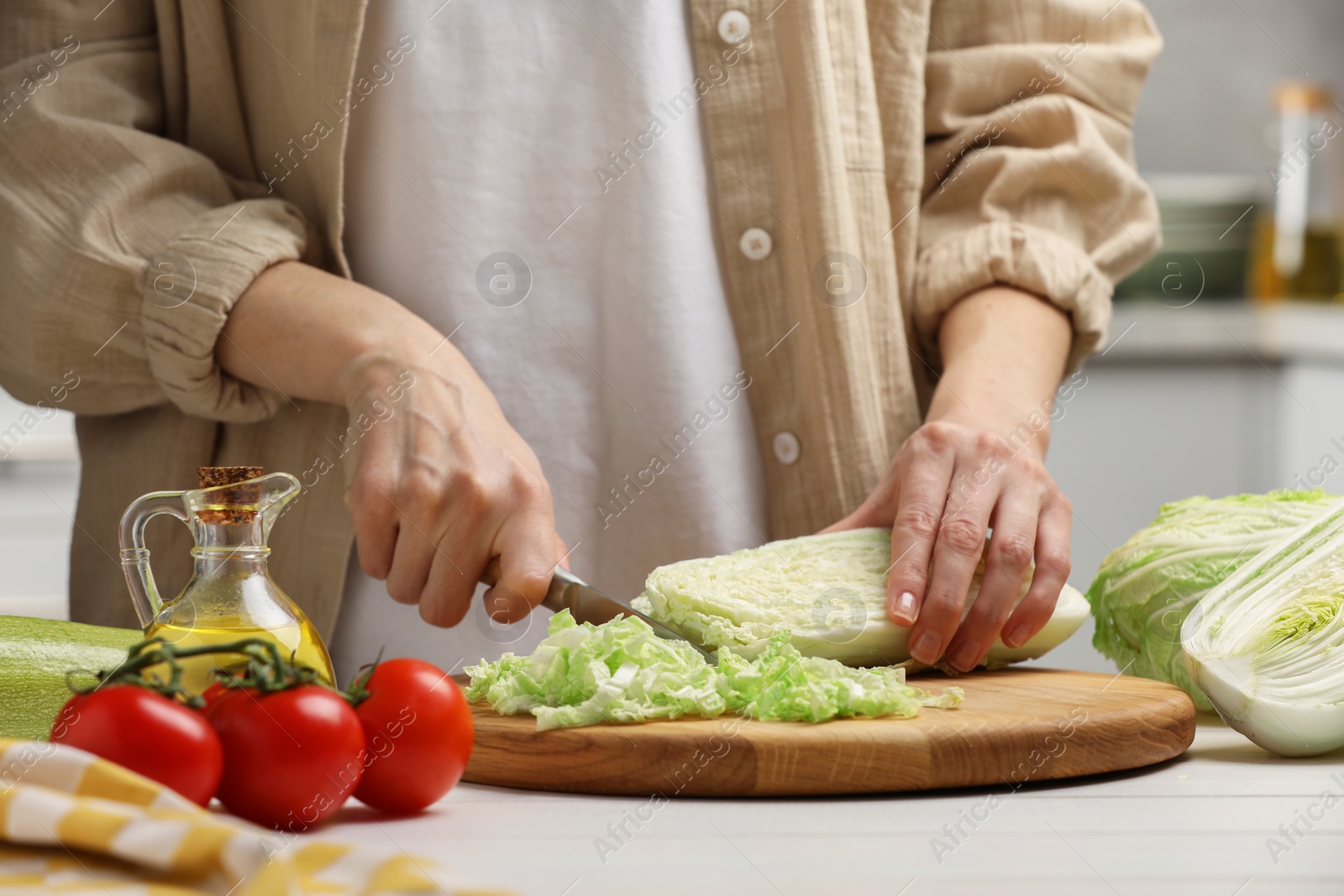 Photo of Woman cutting fresh chinese cabbage at white wooden table in kitchen, closeup