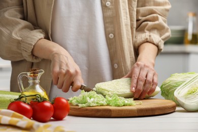 Photo of Woman cutting fresh chinese cabbage at white wooden table in kitchen, closeup