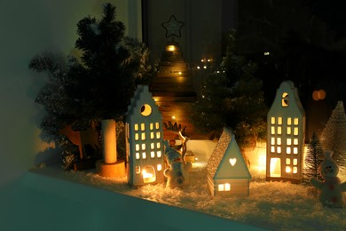 Photo of Christmas atmosphere. Beautiful glowing houses, fir trees and toys on window sill indoor