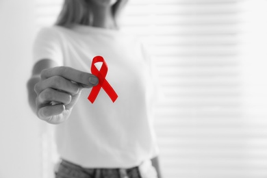 Image of World AIDS disease day. Woman holding red awareness ribbon indoors, closeup 