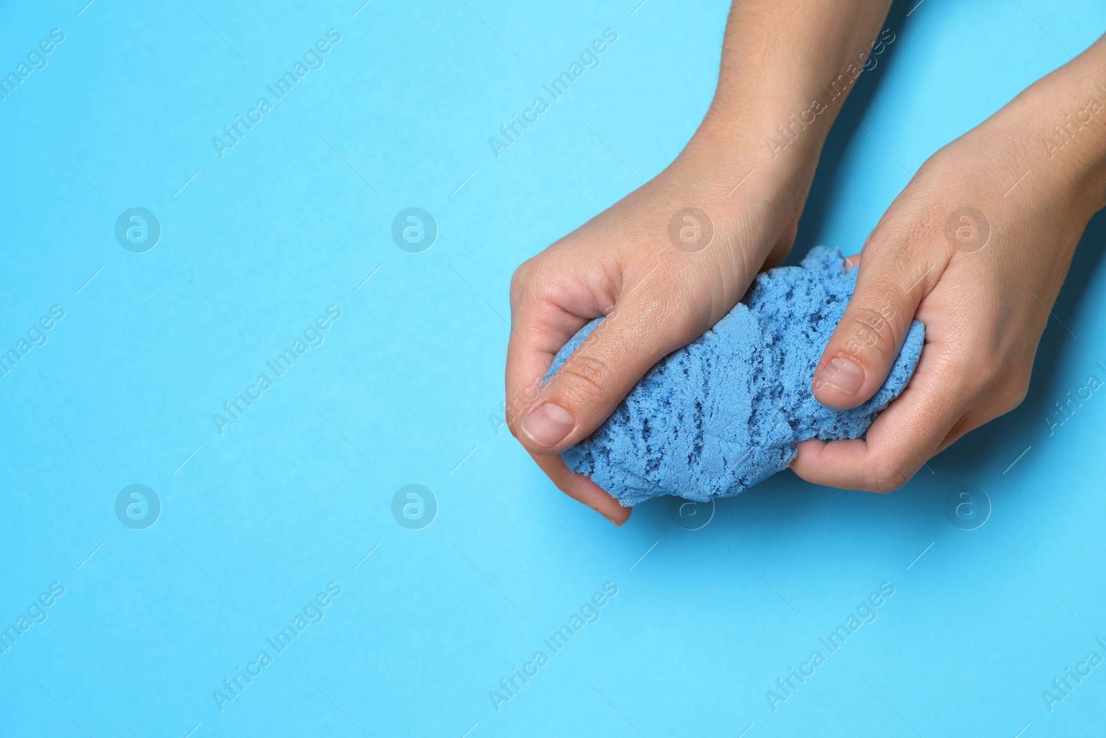 Photo of Woman playing with kinetic sand on light blue background, top view. Space for text
