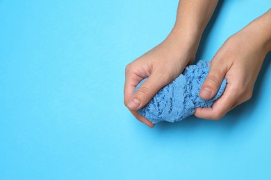 Woman playing with kinetic sand on light blue background, top view. Space for text