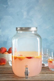 Photo of Peach cocktail in jar with tap on table. Refreshing drink