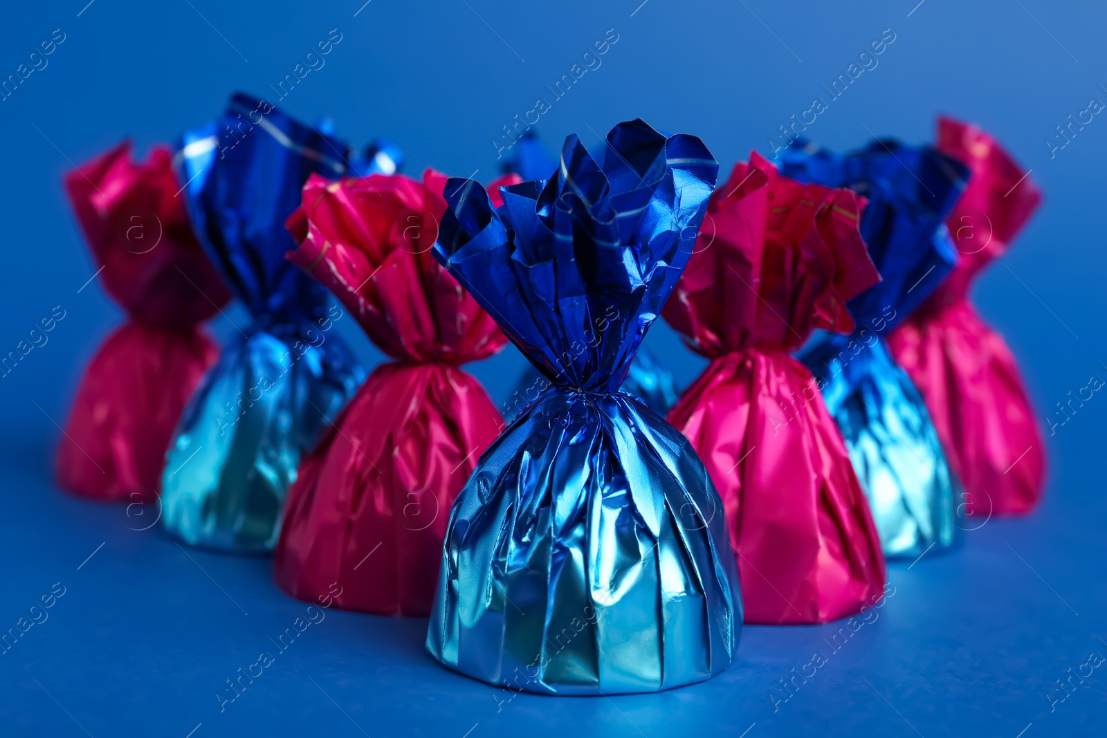 Photo of Candies in colorful wrappers on blue background, closeup