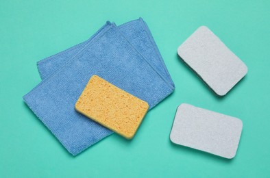 Three color sponges and cloth on turquoise background, top view