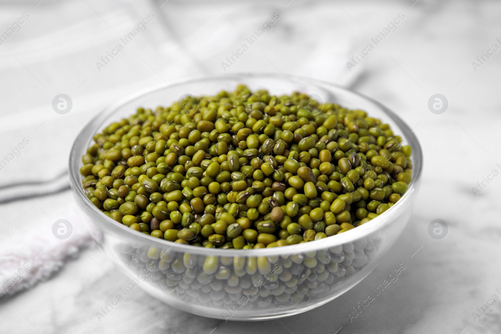 Photo of Glass bowl with green mung beans on white marble table, closeup