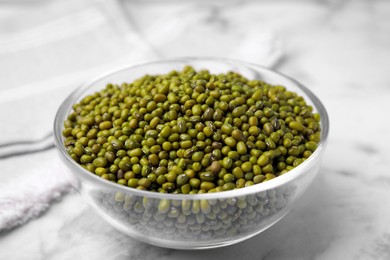 Photo of Glass bowl with green mung beans on white marble table, closeup