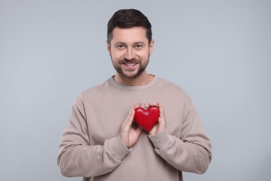 Happy man holding red heart on light grey background