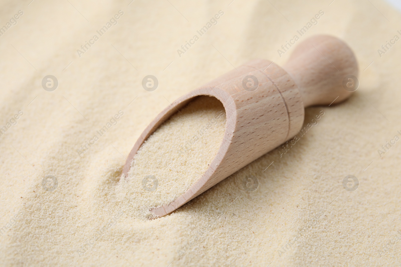 Photo of Uncooked organic semolina and wooden scoop, closeup