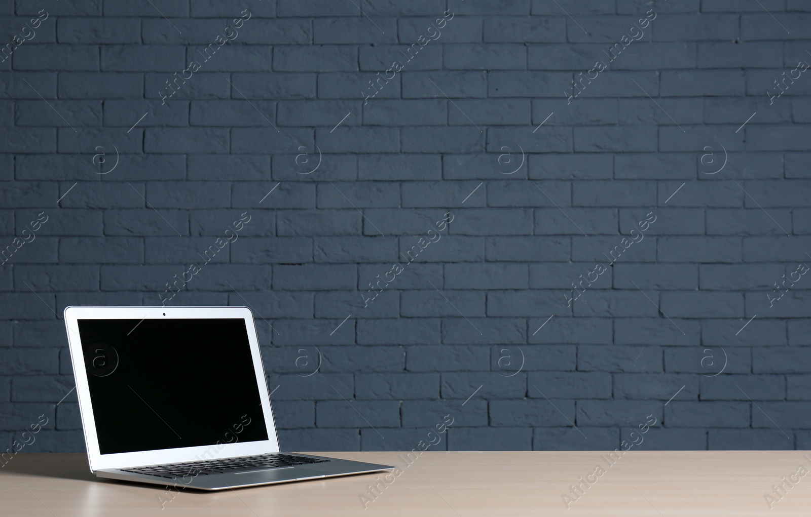 Photo of Modern laptop with blank screen on table against brick wall