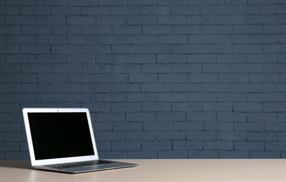 Photo of Modern laptop with blank screen on table against brick wall