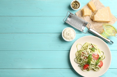 Photo of Delicious zucchini pasta with cherry tomatoes, basil and cheese served on light blue wooden table, flat lay. Space for text