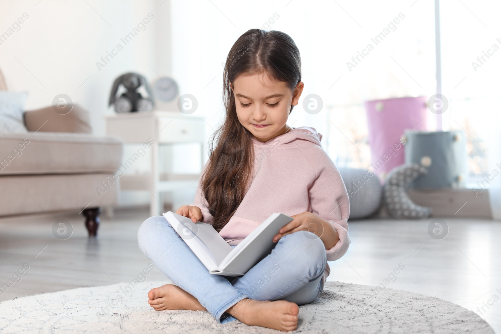 Photo of Cute child reading book on floor indoors