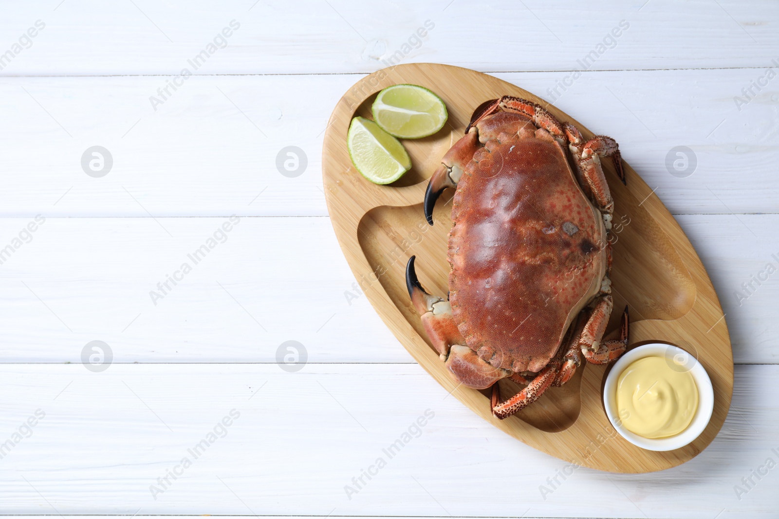 Photo of Delicious boiled crab served with lime and sauce on white wooden table, top view. Space for text