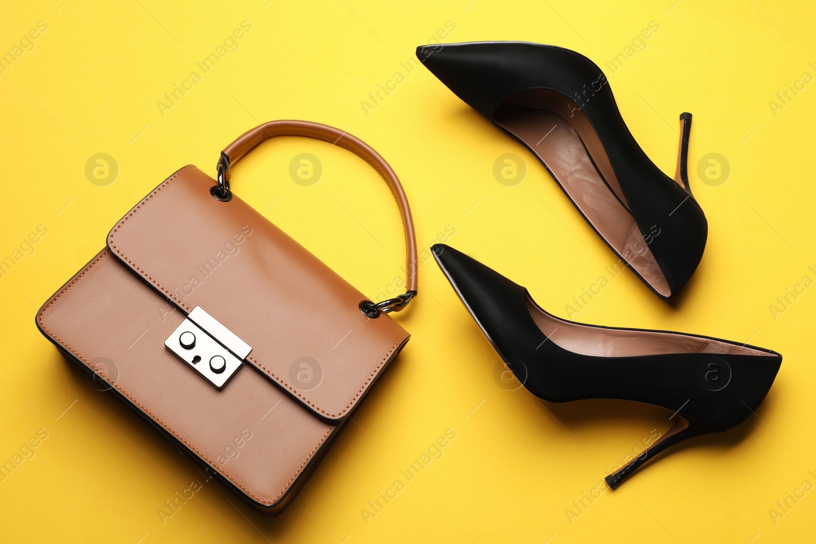 Photo of Pair of elegant high heel shoes and handbag on yellow background, flat lay