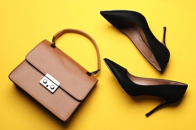 Photo of Pair of elegant high heel shoes and handbag on yellow background, flat lay